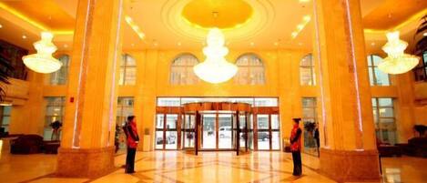 A spacious lobby with a grand chandelier, large columns, and a revolving door.