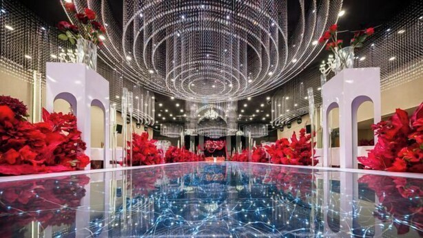 Un interior espacioso y moderno con piso reflectante, diseño simétrico y arreglos florales rojos.