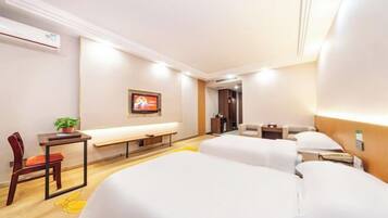 A hotel room with two beds, a desk with a chair, a small table with a plant, a bench, and a framed picture on the wall.