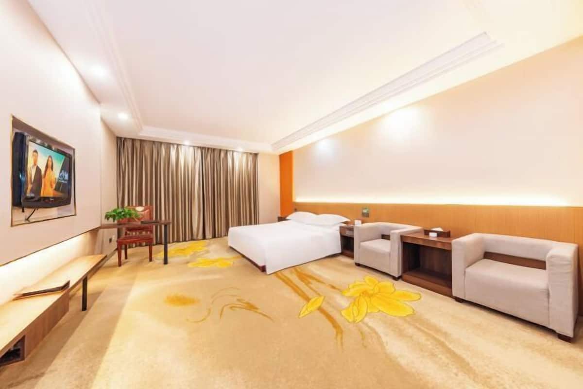 A hotel room with a bed, two sofas, a desk, a bench, and a TV on the wall.