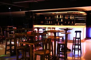Zona de bar con taburetes y mesas, una barra con botellas y un fondo oscuro.