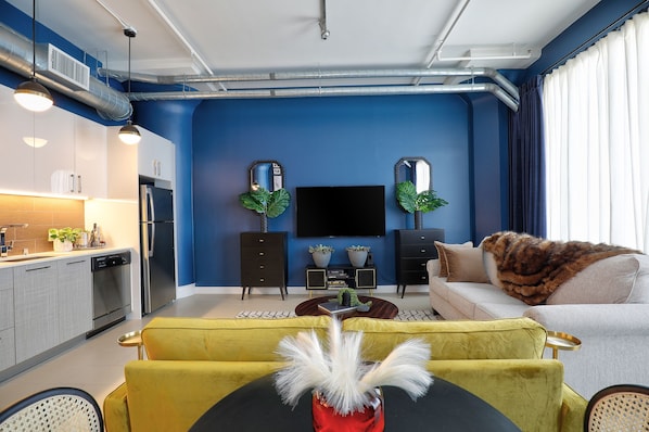 A modern living room with a blue accent wall, a flat-screen TV, a sofa, and a yellow armchair.