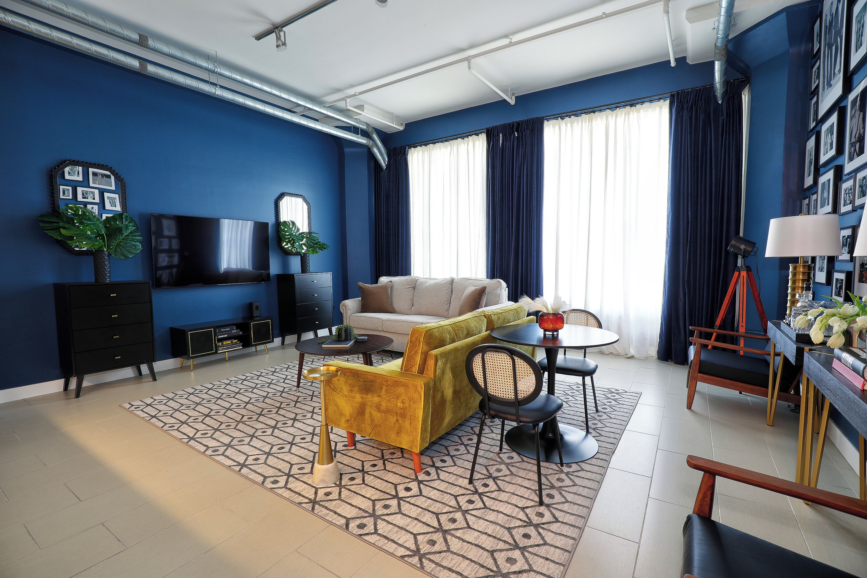 Una sala de estar moderna con pared azul, un sofá, una mesa de centro y un comedor con sillas y una lámpara.