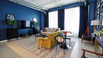Una sala de estar moderna con pared azul, un sofá, una mesa de centro y un comedor con sillas y una lámpara.
