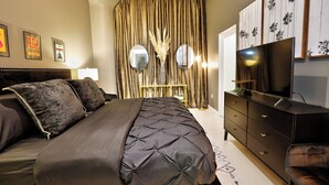 A bedroom with a large bed, a dresser, a TV, and curtains.