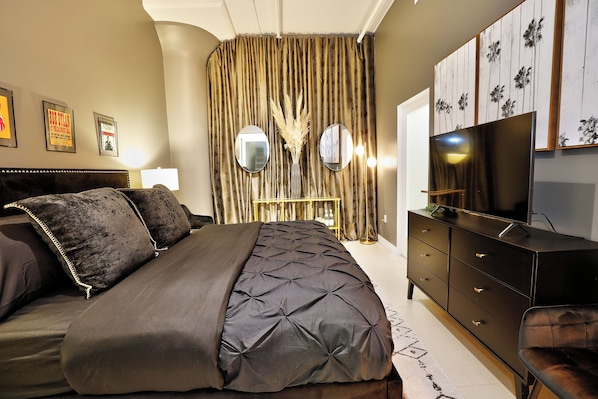 A bedroom with a large bed, a dresser, a TV, and curtains.