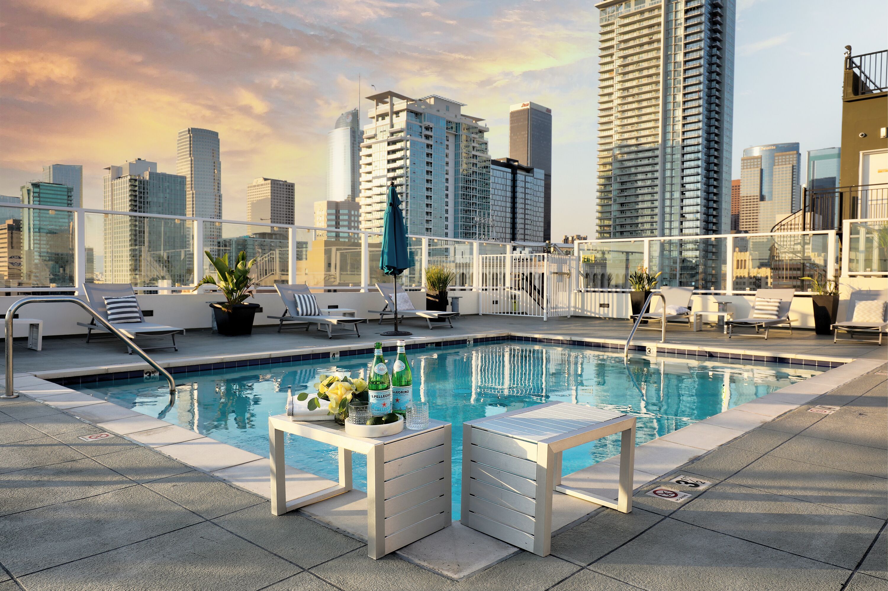 A rooftop pool with lounge chairs and a table, surrounded by high-rise buildings.