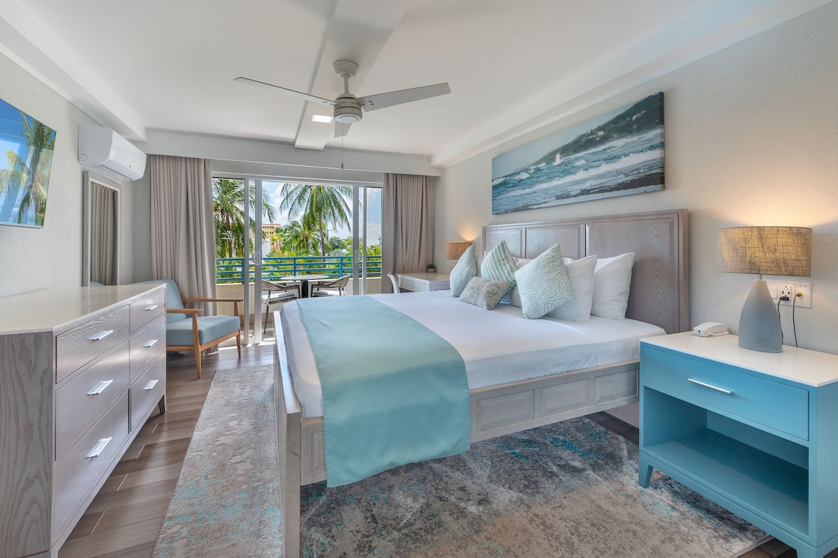 Una habitación de hotel moderna con una cama grande, un escritorio y un balcón con vistas a palmeras.