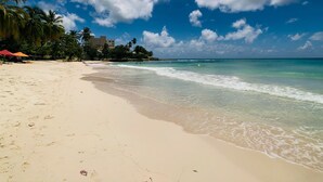 Una playa con aguas azules cristalinas, palmeras y un edificio al fondo.