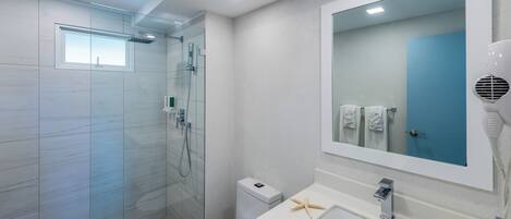 Un baño moderno con ducha envuelta en vidrio, inodoro blanco, lavamanos con espejo y toallero.