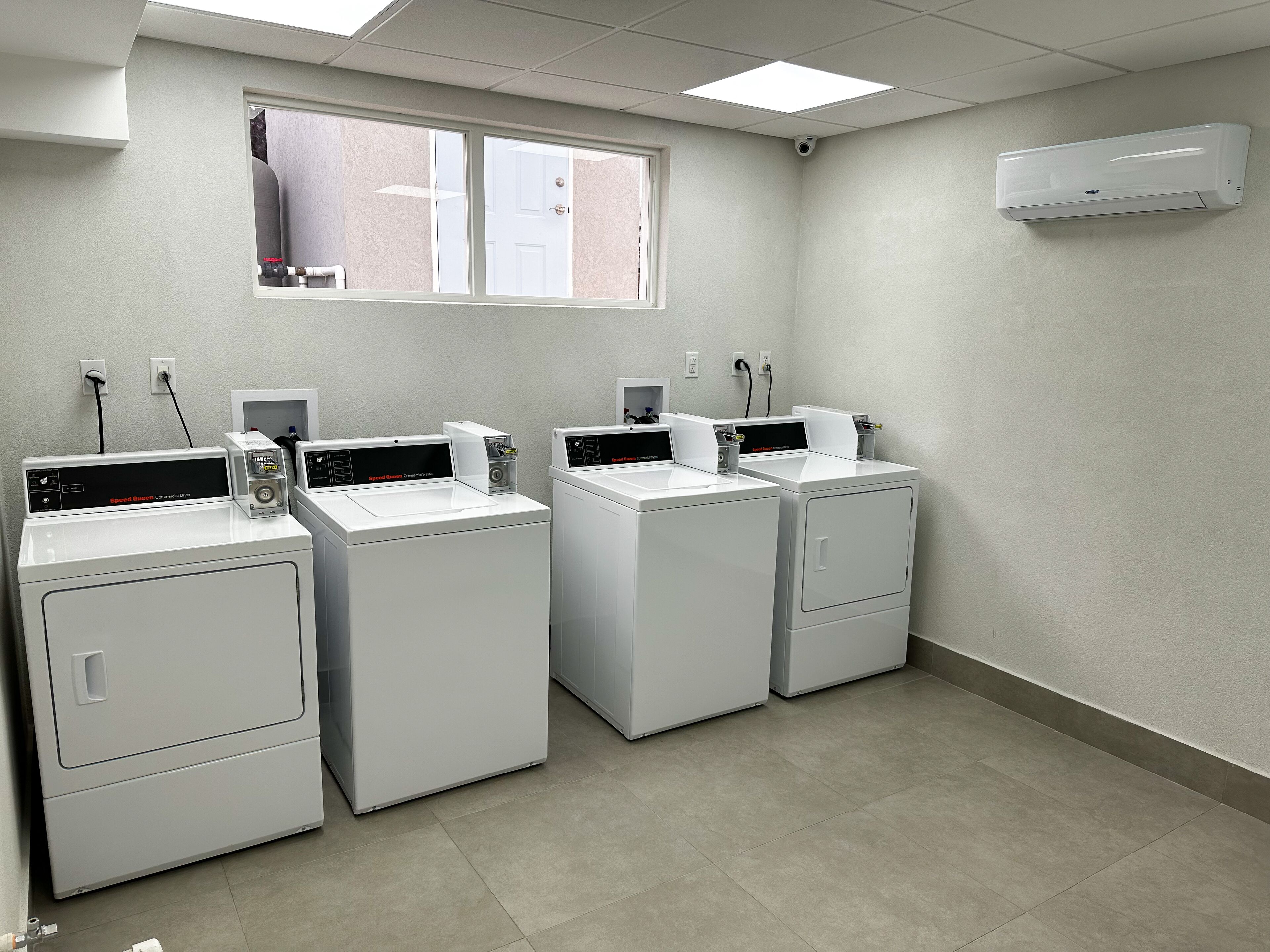 Une buanderie équipée de quatre lave-linge et quatre sèche-linge à chargement frontal, d’une fenêtre et d’un appareil de climatisation.