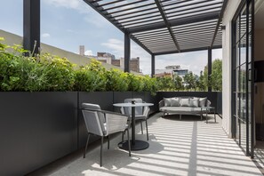 Une terrasse extérieure dotée d’un espace salon moderne, comprenant une table ronde et deux chaises, le tout entouré de verdure et agrémenté d’une structure en forme de pergola.
