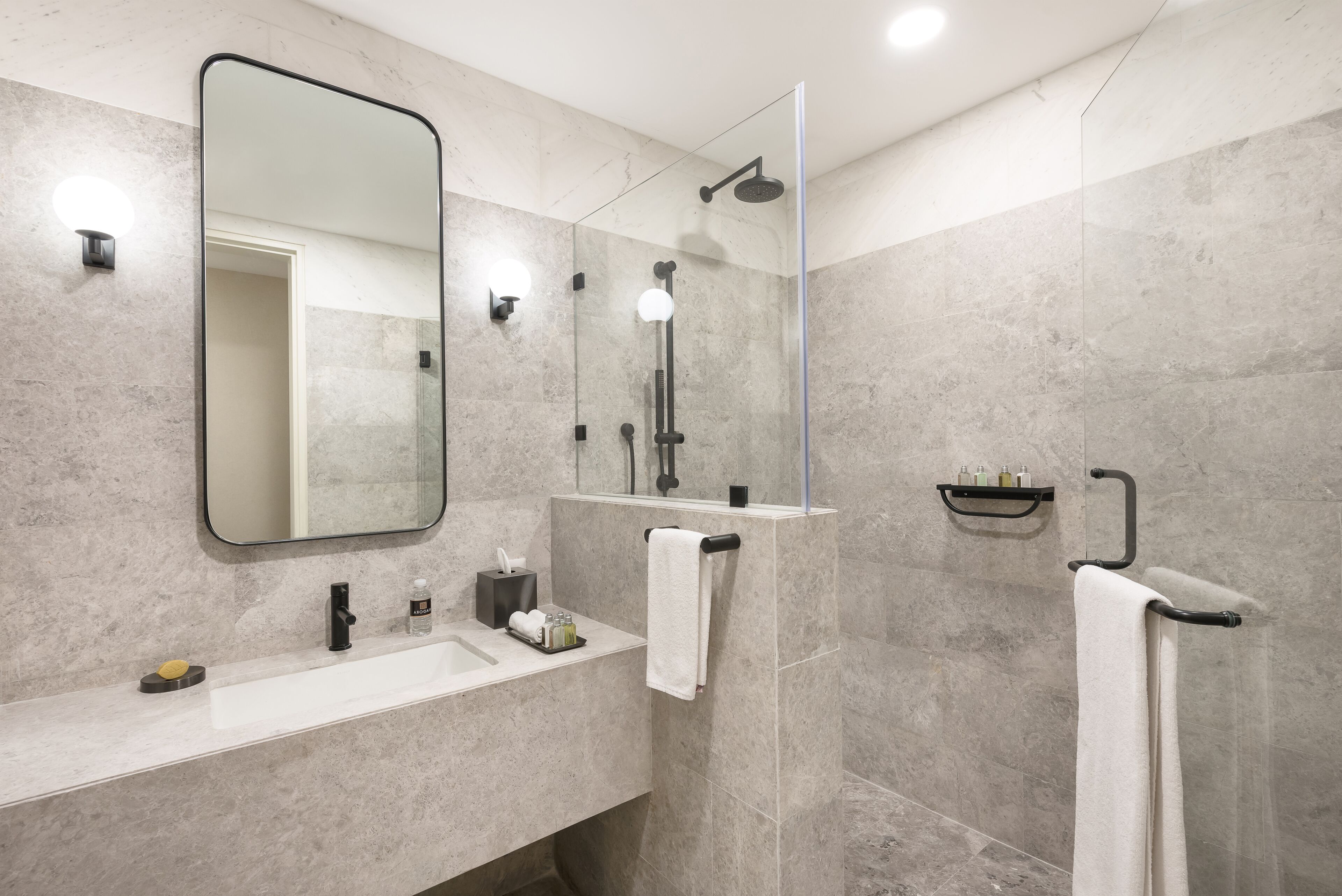 Un bagno moderno con uno specchio grande, una doccia e un lavandino con articoli da toilette.