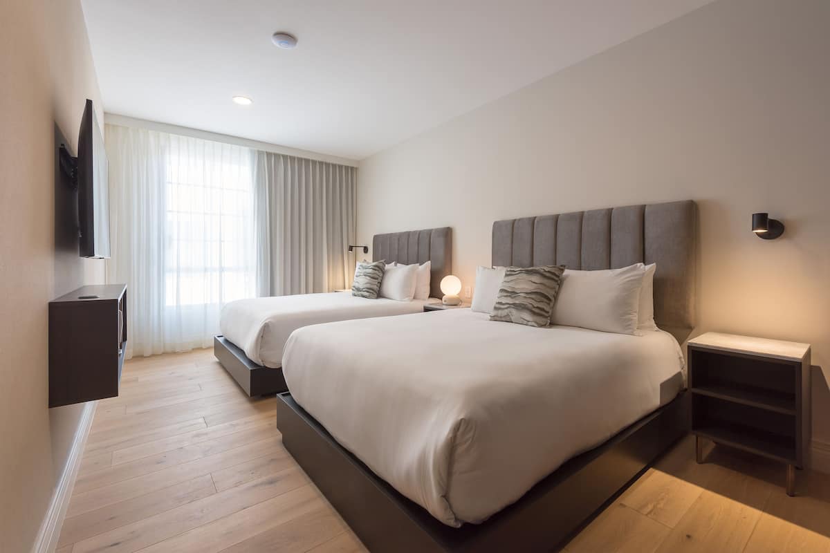 Ein modernes Hotelzimmer mit zwei Betten, einem flachbildfernseher an der Wand und einem großen Fenster mit Vorhängen.