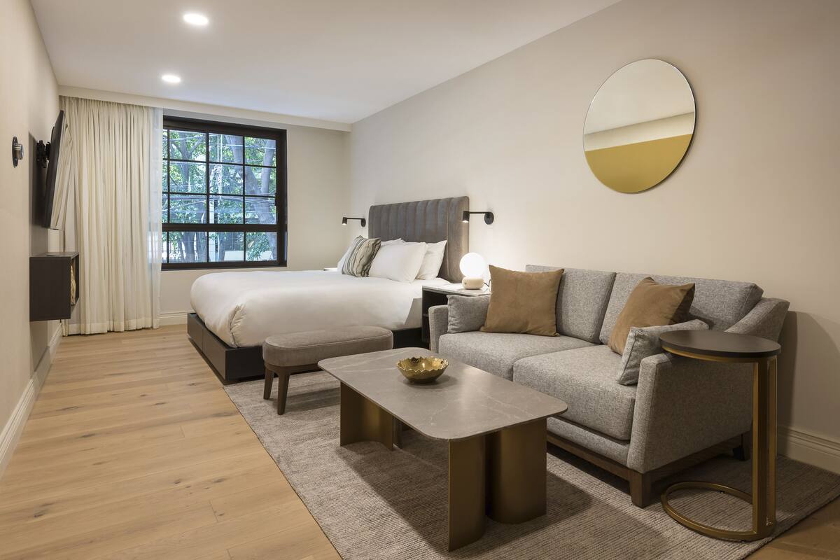 Ein modernes Hotelzimmer mit Bett, Sofa, Couchtisch und einem runden Spiegel.