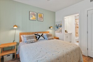 Quarto com uma cama grande, duas mesas de cabeceira com luminárias, um painel de madeira na cabeceira e obras de arte nas paredes.