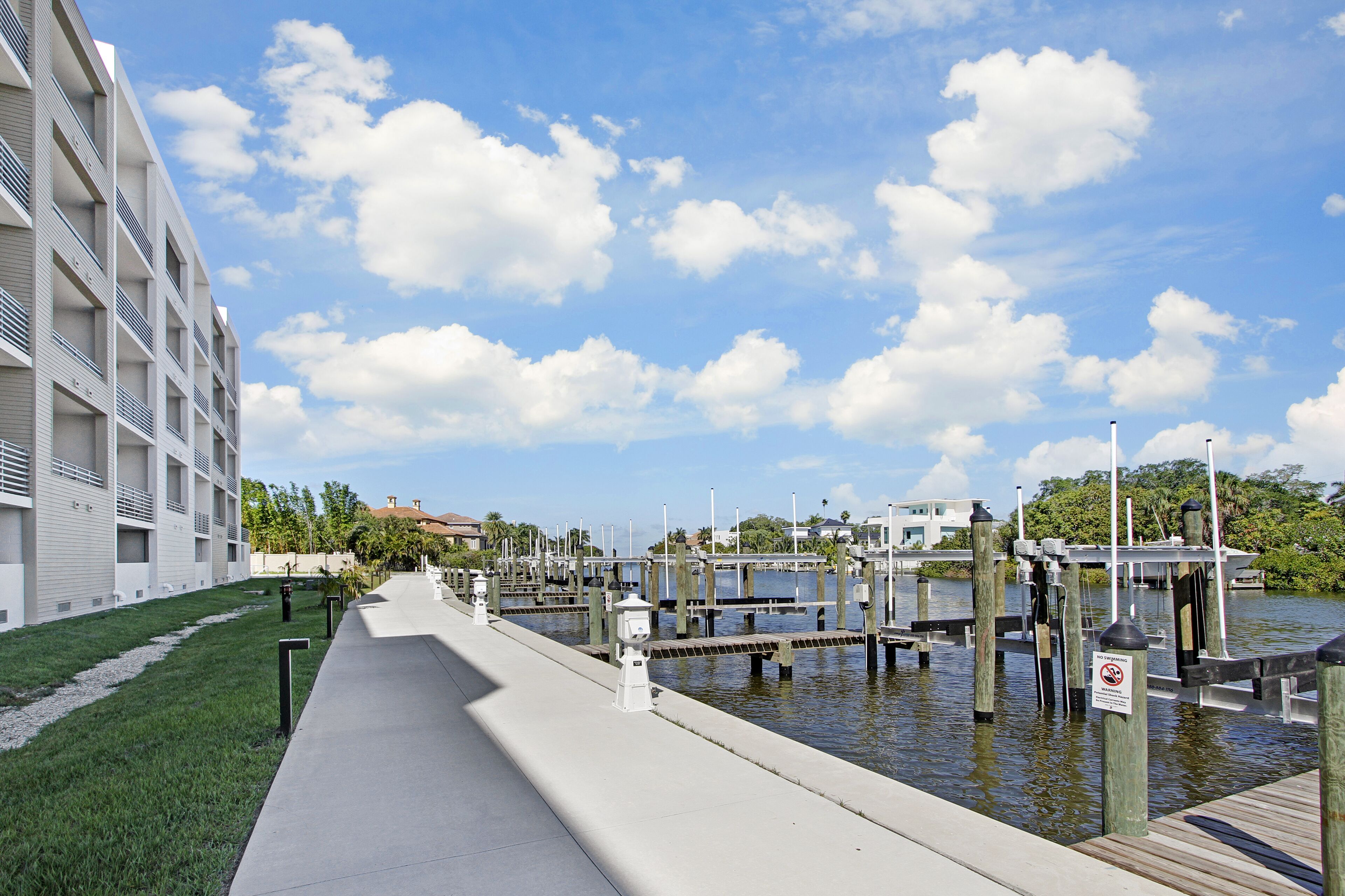 A waterfront walkway with a modern building on one side and a marina with docks.