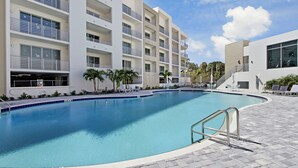 Un hotel moderno con piscina, varios balcones y un cielo azul despejado.