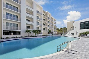 Um hotel moderno com piscina, várias varandas e um céu azul límpido.