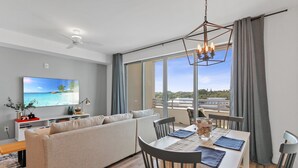 Una sala de estar moderna con un sofá, una mesa de comedor y sillas, un televisor de pantalla plana y un ventanal con vistas.