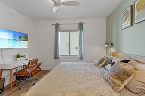 Ett sovrum med en säng, ett skrivbord, en stol, en takfläkt och ett fönster med gardiner.