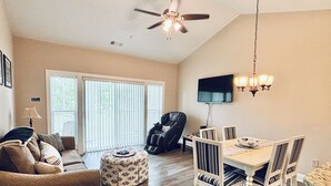 Uma sala de estar ampla, com sofá, apoio para os pés e área de jantar com cadeiras e mesa.