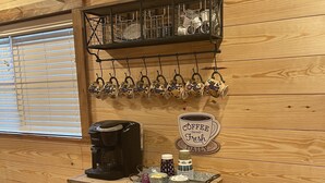 A rustic wooden interior with a coffee station featuring a coffee maker, mugs, and a sign that reads "Coffee Served Fresh Daily."