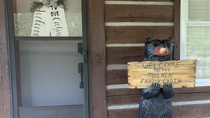 A wooden cabin entrance with a bear statue holding a sign that reads "WELCOME TO THE McLAIN FAMILY CABIN."