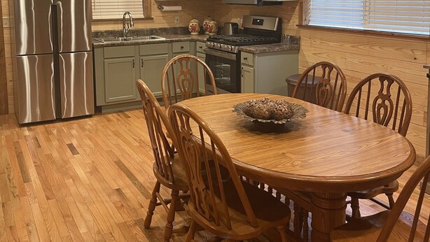 A wooden-paneled kitchen with a stainless steel refrigerator, a microwave, and an oven. There is a dining table with chairs and a decorative centerpiece.