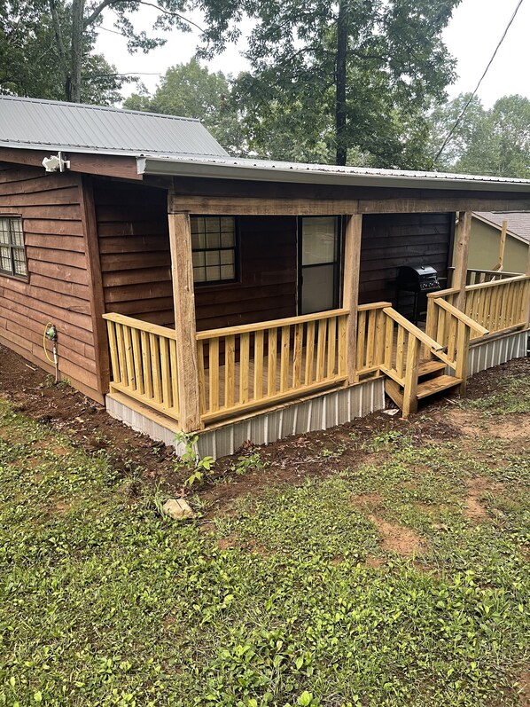 A wooden cabin with a porch, a garage, and a small outdoor area with grass and plants.