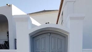 A grey double door with a brass handle, set within a white wall with a stone base. - Raise Spetses Villa Yasemi (Spetses)