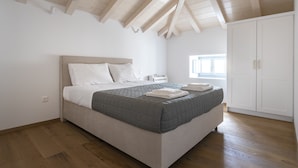 A bedroom with a bed, wooden beams on the ceiling, a window, and a wardrobe. - Raise Spetses Villa Yasemi (Spetses)