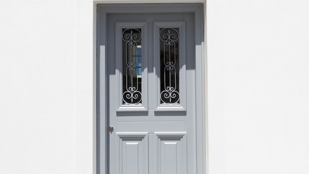 A white building with a symmetrical facade, featuring a central double door with decorative metalwork and a small window above it.