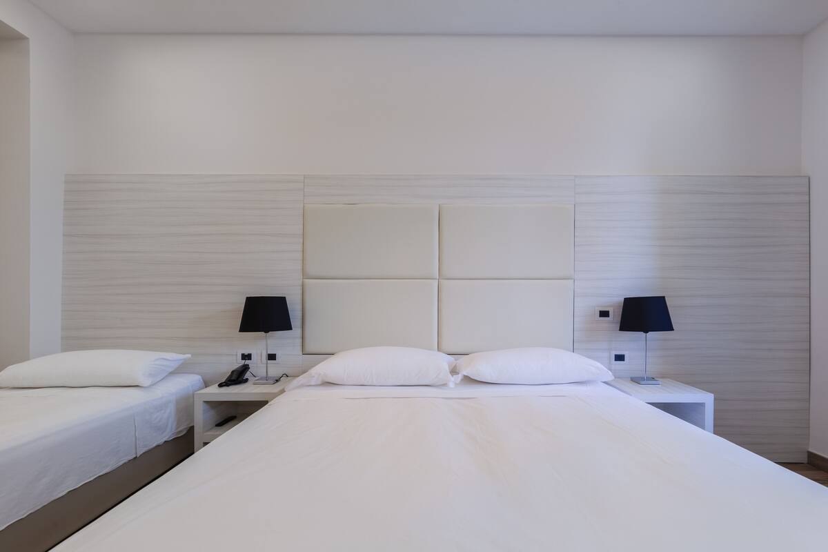 Una habitación de hotel con una cama grande, dos mesitas de noche y dos lámparas.