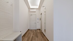 A narrow hallway with a bench, a door, and a mirror on the right wall. - HUB NAPLES (Naples)