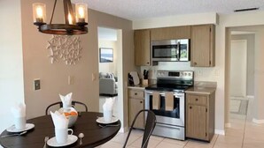 A modern kitchen with stainless steel appliances, wooden cabinets, and a chandelier. - Heated Pool House On Golf Course/7 min from Beach - Discounted (Rotonda West)