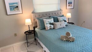 A bedroom with a large bed, two bedside tables with lamps, a window with blinds, and two framed pictures on the wall. - Heated Pool House On Golf Course/7 min from Beach - Discounted (Rotonda West)