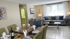 A living room with a sofa, coffee table, and dining area with chairs and a table set for a meal. - Heated Pool House On Golf Course/7 min from Beach - Discounted (Rotonda West)