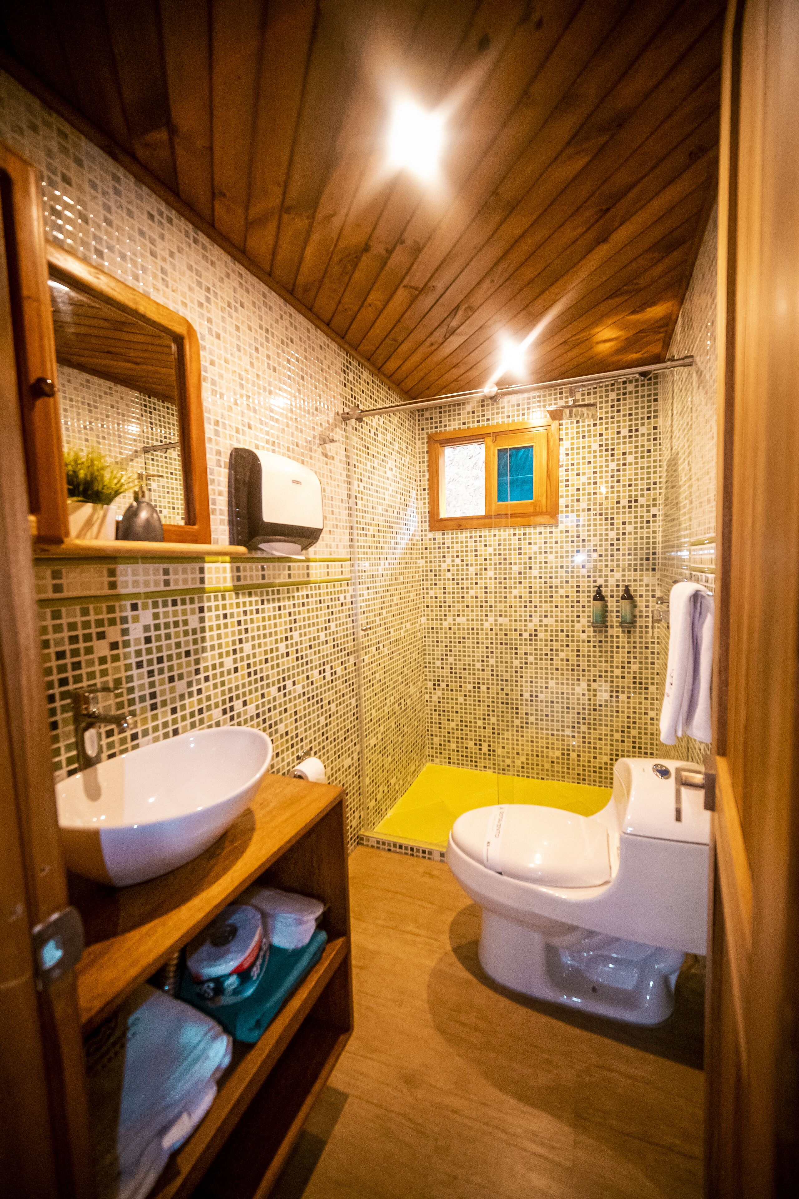 Une salle de bain avec un plafond en bois, un lavabo blanc, des toilettes et un espace douche.