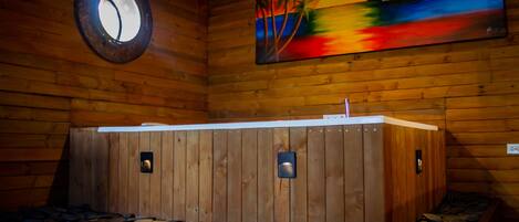 A wooden sauna with a stone floor, a painting of a sunset, and a round window.