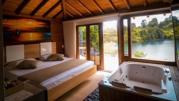Ein Schlafzimmer mit Holzbalkendecke, einem Bett, einer Badewanne und Seeblick.