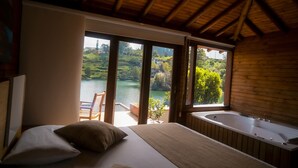 Ein Schlafzimmer mit einem großen Bett, einer Badewanne und Blick auf einen See.