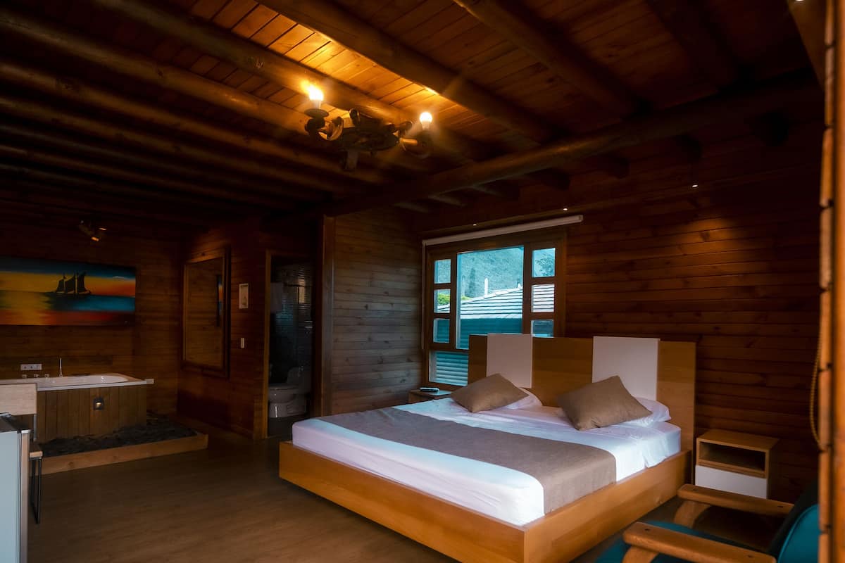 A wooden cabin bedroom with a large bed, a wooden desk, and a bathtub.