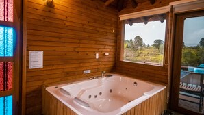 Eine Holzhütte mit einer großzügigen Badewanne, einem Fenster mit Aussicht und einer Holzbalkendecke.