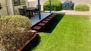 Un espace patio avec une table et des chaises, une petite pelouse et un mur en briques.