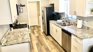 Une cuisine moderne avec des meubles blancs, des plans de travail en granit, un réfrigérateur en acier inoxydable et un parquet en bois disposé en motif chevron.