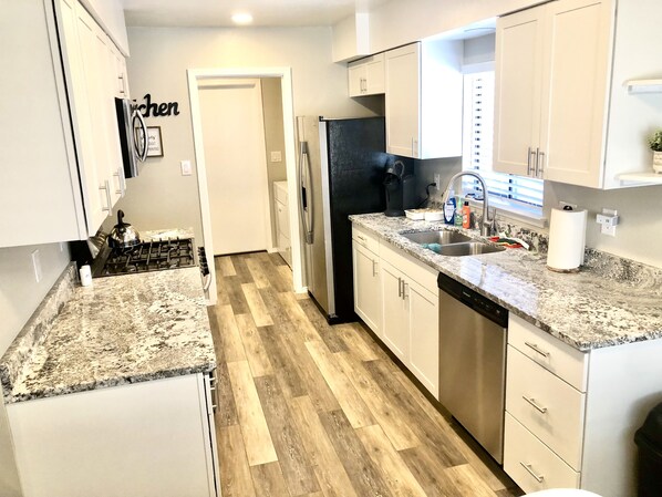 A modern kitchen with white cabinets, granite countertops, a stainless steel refrigerator, and a wooden herringbone floor. - Beautiful newly remodeled 3 bed 2 bath foothills home.  No cleaning fees. (Albuquerque)