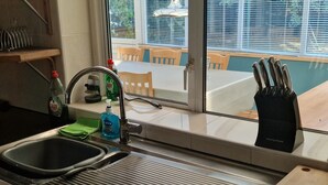 A kitchen with a double sink, a window with a view of a dining area, and a knife block on the counter.