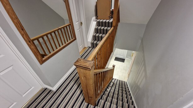 A staircase with wooden railings and striped carpet.