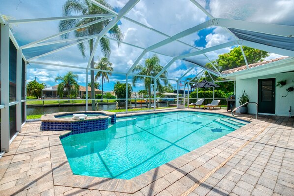 Una piscina con un porche techado, un jacuzzi y vistas a palmeras y un lago.
